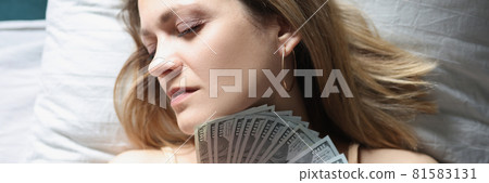 Young woman sleeping in bed with dollar bills in her hands Young woman sleeping in bed with dollar bills in her hands 81583131