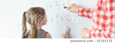 Little girl and teacher solving math equations on blackboard Little girl and teacher solving math equations on blackboard 81583178