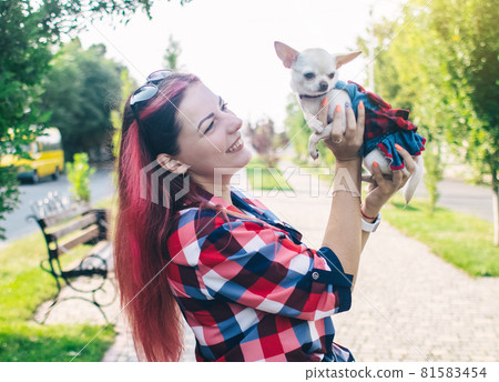 The girl holds a mini chihuahua in her arms. Kissing your pet. The dog and the owner are dressed in the same color. Clothes for animals. Love and care for four-legged pets. 81583454