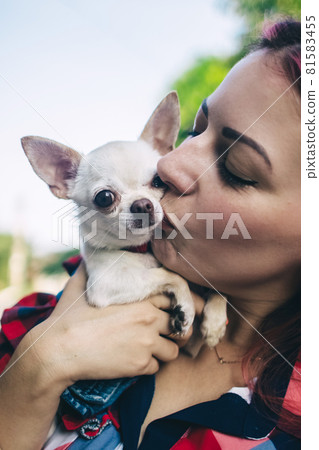 The girl holds a mini chihuahua in her arms. Kissing your pet. The dog and the owner are dressed in the same color. Clothes for animals. Love and care for four-legged pets. The girl holds a mini chihuahua in her arms. Kissing your pet. The dog and the owner are dressed in the same color. Clothes for animals. Love and care for four-legged pets. 81583455