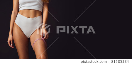Cropped body. Slim tanned beautiful woman in underwear isolated over dark brown background. 81585384
