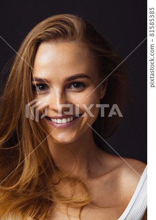 Close-up portrait of young beautiful smiling caucasian woman isolated over dark brown studio background 81585385