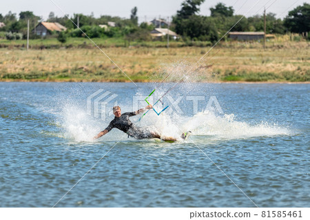 Young adult caucasian fit male person enjoy riding kite surf board in sun uv protection suit on bright sunny day against blue sky at sea or ocean shore. Watersport adrenaline fun adventure acitivity 81585461