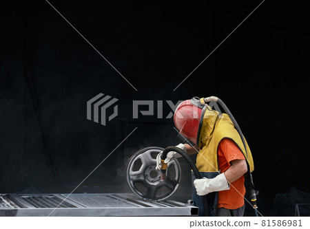 Man in uniform using sandblaster for polishing metal 81586981