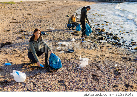 Dedicated woman in a team picking up plastic garbage in bag at beach Dedicated woman in a team picking up plastic garbage in bag at beach 81589142