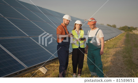 An employee of a solar power plant talks on a walkie-talkie while his colleagues and an investor check the solar power plant with an infrared scanner, a drone. Photovoltaic solar panel installation 81589651