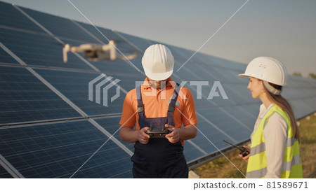 Industrial expert wearing helmet and controlling drone in photovoltaic solar power plant. Solar panel array installation. Technologies and ecology. Female investor checks the work Industrial expert wearing helmet and controlling drone in photovoltaic solar power plant. Solar panel array installation. Technologies and ecology. Female investor checks the work 81589671