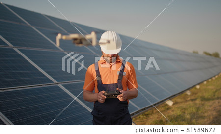 Industrial expert wearing helmet and controlling drone in photovoltaic solar power plant. Solar panel array installation. Technologies and ecology. Female investor checks the work 81589672