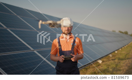 Industrial expert wearing helmet and controlling drone in photovoltaic solar power plant. Solar panel array installation. Technologies and ecology. Female investor checks the work Industrial expert wearing helmet and controlling drone in photovoltaic solar power plant. Solar panel array installation. Technologies and ecology. Female investor checks the work 81589673