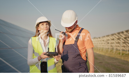 Technician and investor Using Infrared Drone Technology to Inspect Solar Panels in Solar cell Farm. Engineer woman in hardhat holding tablet computer operating flying drone in solar plant 81589687