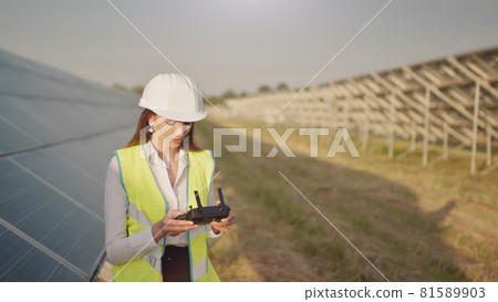 Engineer woman in hardhat holding tablet computer operating flying drone in solar plant. Photovoltaic solar panel installation. Solar array. New technologies. The investor checks the solar power Engineer woman in hardhat holding tablet computer operating flying drone in solar plant. Photovoltaic solar panel installation. Solar array. New technologies. The investor checks the solar power 81589903