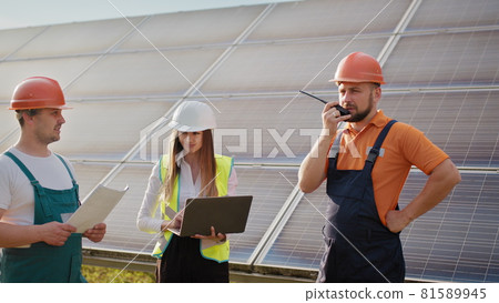 Team of industrial colleagues using tablet monitoring rows of photovoltaic solar panels at sunset. Business cooperation. Solar park. Alternative energy concept. Clean energy 81589945