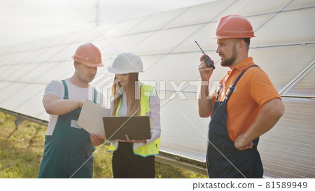 Team of industrial colleagues using tablet monitoring rows of photovoltaic solar panels at sunset. Business cooperation. Solar park. Alternative energy concept. Clean energy 81589949