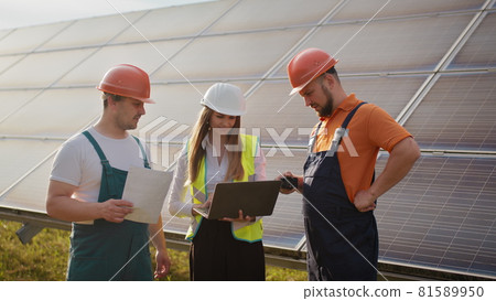 Three solar energy specialists walking at a solar power facility. Professional engineers discuss innovative project. Business team. Clean energy. Professional engineers discuss innovative project 81589950