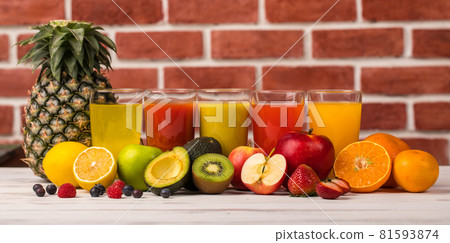 Different fruits juice in glass, apple, orange and strawberry juice with straw, looking refreshing on colourful wood board in front of brick wall background. Picture decorating with fresh fruits 81593874