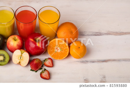 Different fruits juice in glass, apple, orange and strawberry juice with straw, looking refreshing on colourful wood board in front of white wall background. Picture decorating with fresh fruits 81593880