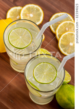 Two refreshing glasses of cold fruit juice with straw, ice lime and lemon juice, decorating with fresh lime and lemon on wooden table. Concept for refreshing Two refreshing glasses of cold fruit juice with straw, ice lime and lemon juice, decorating with fresh lime and lemon on wooden table. Concept for refreshing 81594023