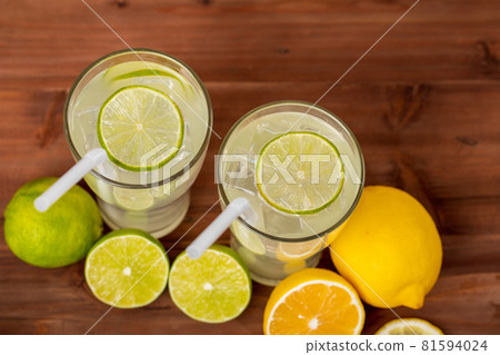 Two refreshing glasses of cold fruit juice with straw, ice lime and lemon juice, decorating with fresh lime and lemon on wooden table. Concept for refreshing 81594024