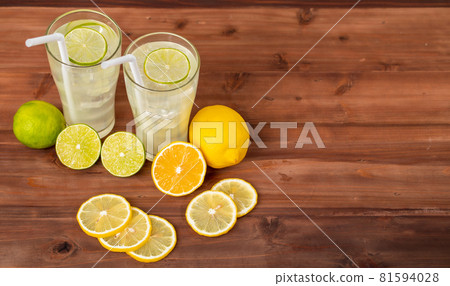 Two refreshing glasses of cold fruit juice with straw, ice lime and lemon juice, decorating with fresh lime and lemon on wooden table. Concept for refreshing Two refreshing glasses of cold fruit juice with straw, ice lime and lemon juice, decorating with fresh lime and lemon on wooden table. Concept for refreshing 81594028