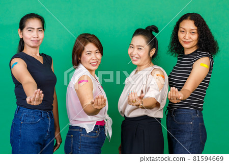 Four middle aged Asian women showing their arms with bandage patch showing they got vaccinated for Covid 19 virus on green background. Concept for Covid 19 vaccination 81594669