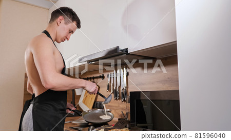 man with a naked torso and in a black apron prepares pancakes in kitchen 81596040