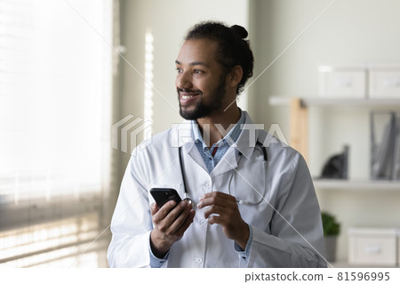 Dreamy young african american doctor holding cellphone in hands. 81596995