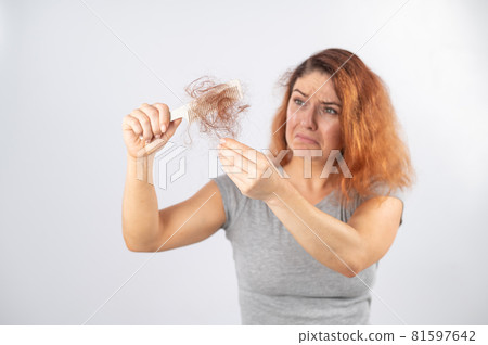 Caucasian woman with a grimace of horror holds a comb with a bun of hair. Hair loss and female alopecia. Caucasian woman with a grimace of horror holds a comb with a bun of hair. Hair loss and female alopecia. 81597642