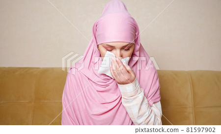 Beautiful muslim woman in hijab coughs and freezes while sitting on the sofa 81597902