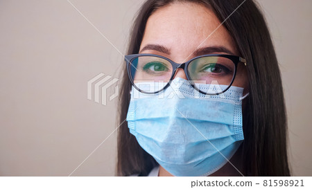 Close up of young brunette woman doctor with glasses and light blue protective mask 81598921