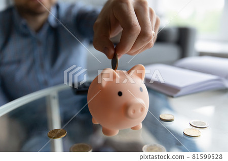Millennial man inserting coin into piggy bank Millennial man inserting coin into piggy bank 81599528