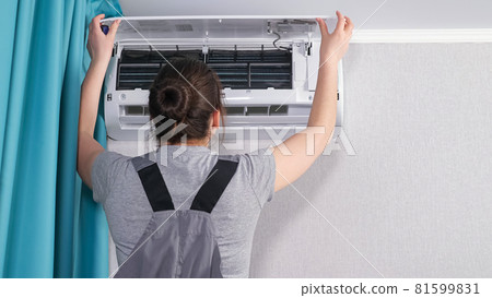 Woman in workwear opens white air conditioner unit cover 81599831