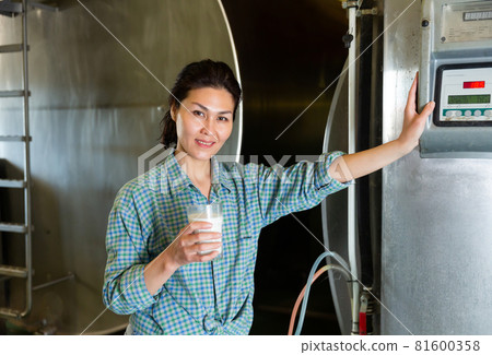 Portrait of a smiling asian woman standing in a dairy farm with a glass of milk Portrait of a smiling asian woman standing in a dairy farm with a glass of milk 81600358