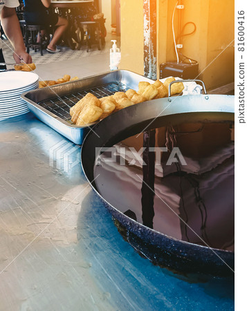 Dough sticks or deep-fried Chinese dough called patongo for sale on tray near large frying pan. Patongo is a deep-fried dough stick. Famous traditional asian breakfast street food. Selective focus. 81600416