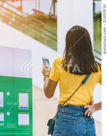 Back view of female customer wear face mask registering with smartphone and scan QR CODE via SafeEntry to check-in during the outbreak of Corona virus(Covid-19) at the entrance gate.New normal concept 81600816
