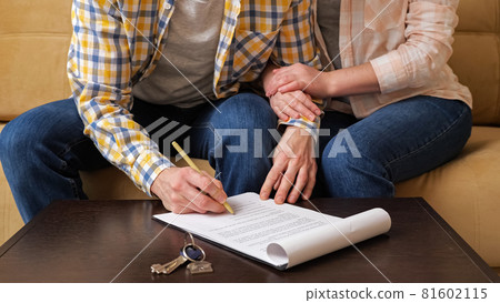Husband signs apartment purchase contract near wife on sofa Husband signs apartment purchase contract near wife on sofa 81602115