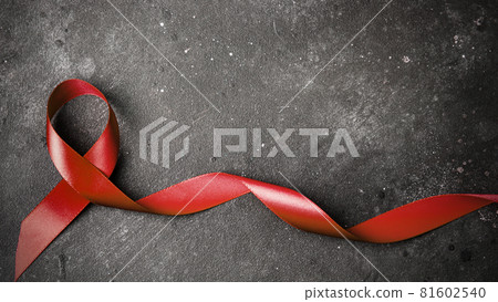 The red ribbon on a dark gray background. The symbol of The World AIDS Day or cancer or HIV Awareness Month and concept of healhcare. Copy space The red ribbon on a dark gray background. The symbol of The World AIDS Day or cancer or HIV Awareness Month and concept of healhcare. Copy space 81602540