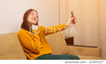 Young brunette holds smartphone and poses into front camera Young brunette holds smartphone and poses into front camera 81604227