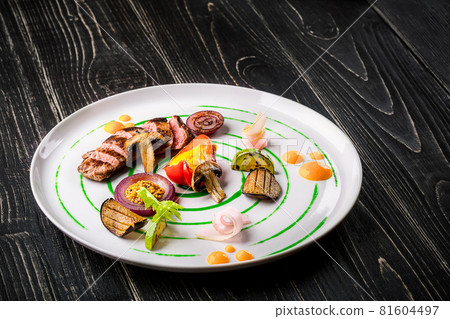 Sliced meat with fresh herbs, vegetables and spices on a white plate on a black wooden background, top view 81604497
