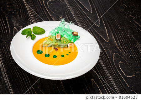 A bowl with pumpkin soup on a black wooden background. Firm feed from the chef 81604523
