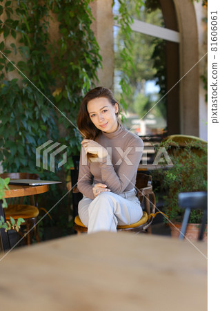 Young caucaisian woman posing at street cafe, closed laptop computer on table. 81606061