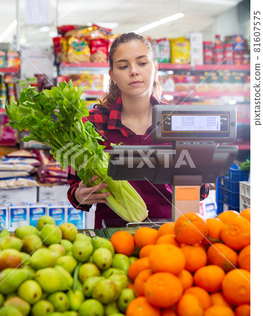 Young saleswoman weighs greens on a scale Young saleswoman weighs greens on a scale 81607575
