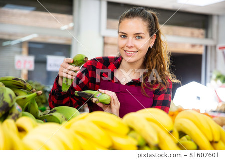 Portrait of a positive young saleswoman checking bananas on the counter 81607601