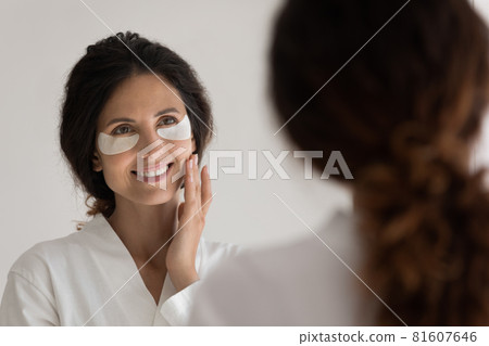 Happy young woman applying patches under eyes. Happy young woman applying patches under eyes. 81607646