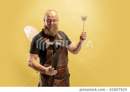 Comic portrait of muscular bearded bald man, blacksmith in leather apron or uniform isolated on yellow studio background. Concept of labor, retro professions, power, strength, humor Comic portrait of muscular bearded bald man, blacksmith in leather apron or uniform isolated on yellow studio background. Concept of labor, retro professions, power, strength, humor 81607929