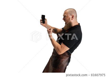 Comic portrait of muscular bearded bald man, blacksmith in leather apron or uniform isolated on white studio background. Concept of labor, retro professions, power, beauty, humor 81607975