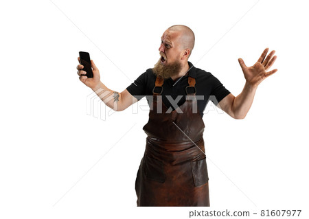 Comic portrait of muscular bearded bald man, blacksmith in leather apron or uniform isolated on white studio background. Concept of labor, retro professions, power, beauty, humor Comic portrait of muscular bearded bald man, blacksmith in leather apron or uniform isolated on white studio background. Concept of labor, retro professions, power, beauty, humor 81607977