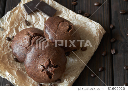A group of homemade chocolate muffins on parchment with coffee beans and pieces of chocolate. Dark wooden background, closeup, selective focus 81609020