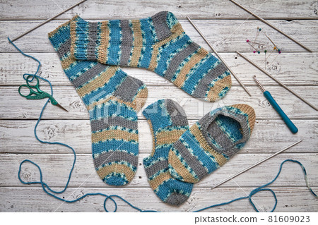 Two children's knitted socks and slippers on a light wooden background 81609023