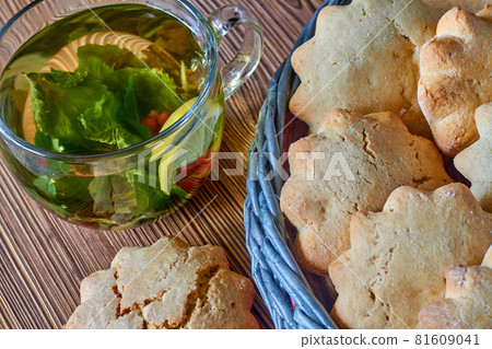 Biscuits in the wicker basket from newspaper tubules and a transparent cup of silverqueen green tea with mint and red currants on brown wooden background. Closeup, selective focus 81609041
