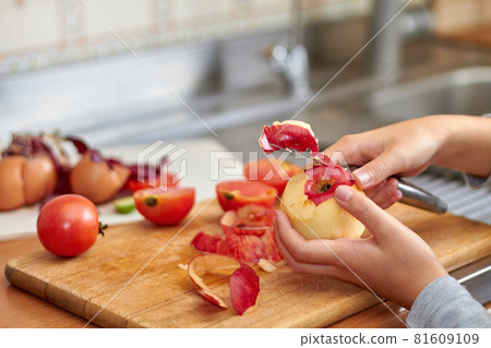 The girl cuts a peel with a knife from a red apple. Food waste and offcuts while preparing food on the kitchen. Closeup, selective focus 81609109